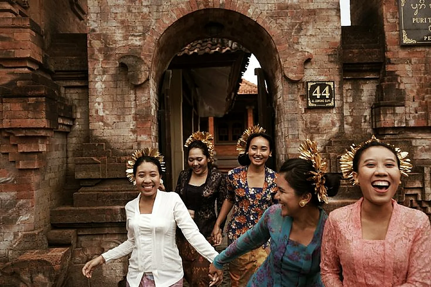 Balinese women laughing as they walk out of a brick temple gate